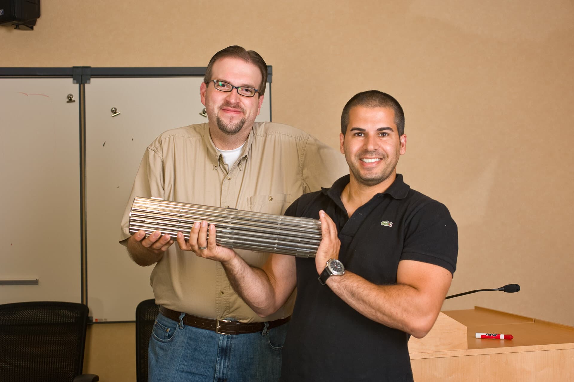 Two TWG team members holding a full-scale model of a used nuclear fuel bundle in a meeting room.